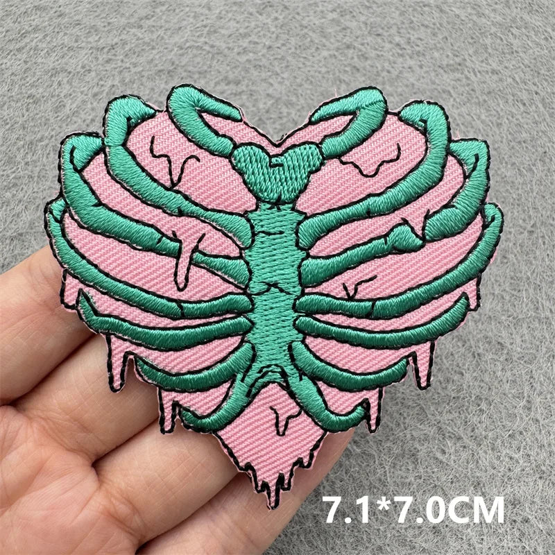 Pink and green skeleton ribcage patch held by a hand on a gray background