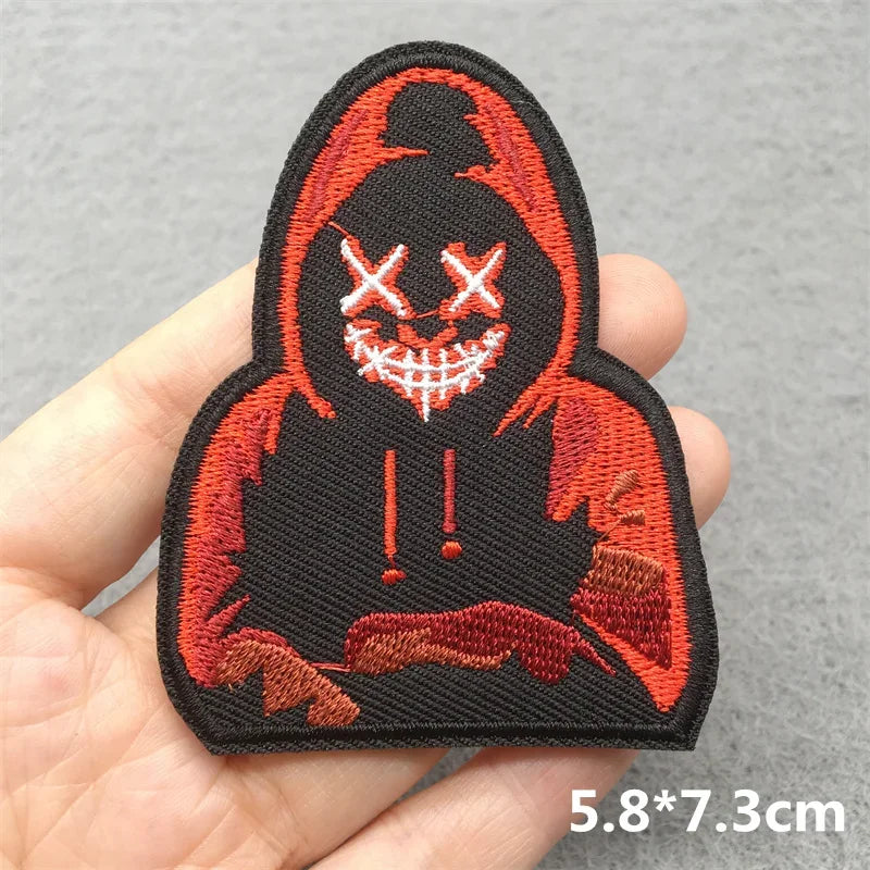 Embroidered patch with a hooded figure design held in a hand on a gray background