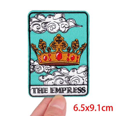 Patch with a crown design and 'The Empress' text on a blue background, held by a hand.