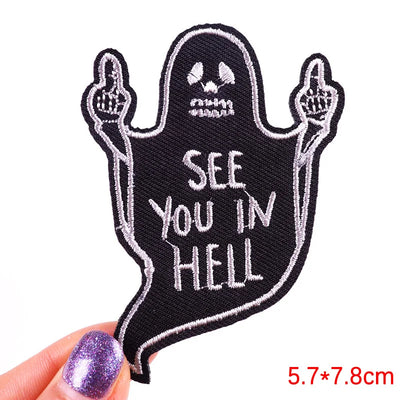 Ghost-shaped patch with 'See You in Hell' text held by a hand with purple nail polish on a white background.