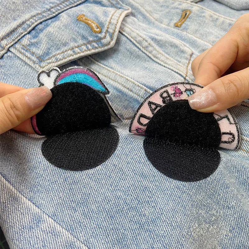 Black Velcro patches held over a denim jacket with colorful patches.