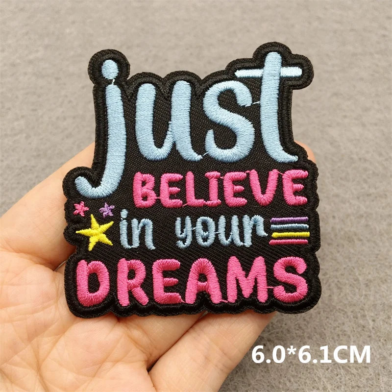 Embroidered patch with 'Just Believe in Your Dreams' text held by a hand on a neutral background.