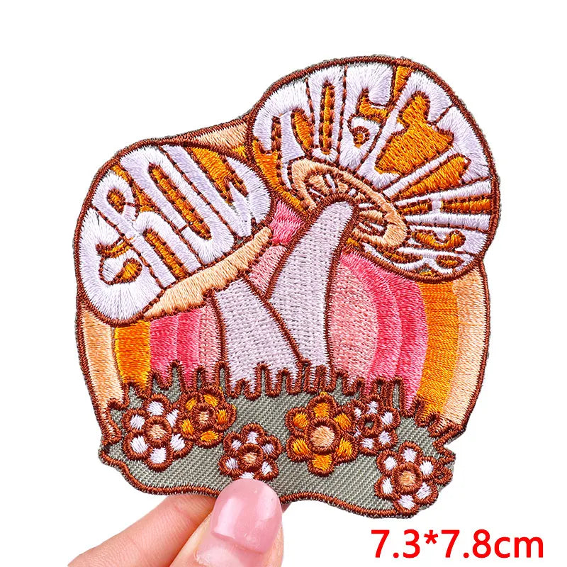 Embroidered patch with a mushroom design held by a hand, on a white background.
