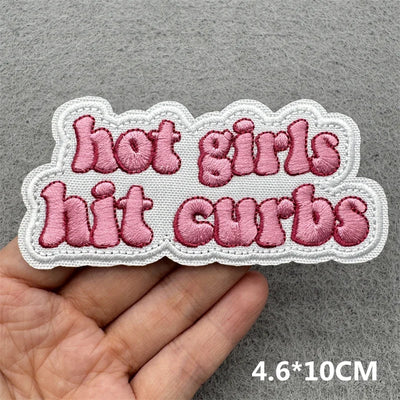 Embroidered patch with text 'hot girls hit curbs' held by a hand on a gray background.