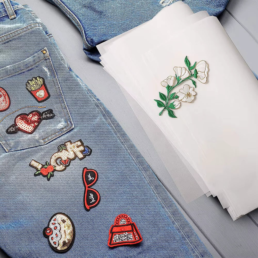 Denim fabric with various patches and a piece of iron on adhesive sheets with floral design on a gray surface