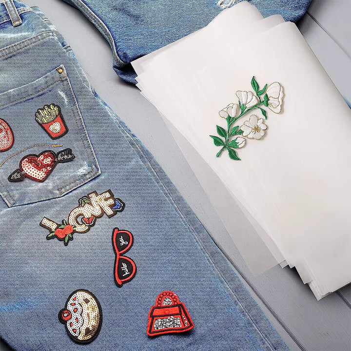 Denim fabric with various patches and a piece of iron on adhesive sheets with floral design on a gray surface