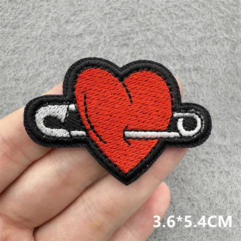 Heart-shaped safety pin patch held by a hand on a gray background