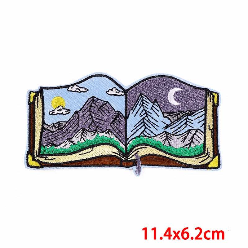 Embroidered patch of an open book with mountain scenes on a white background
