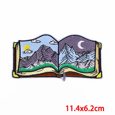 Embroidered patch of an open book with mountain scenes on a white background