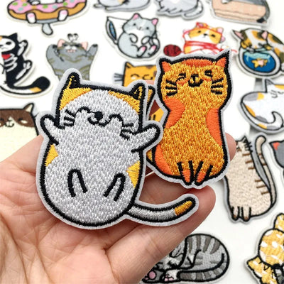Collection of cat-themed embroidered patches held by a hand with more patches in the background.