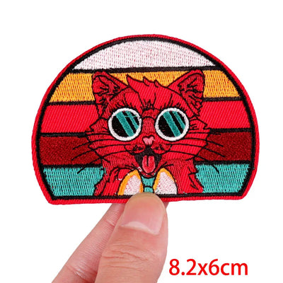 Colorful embroidered patch of a cat with a striped background held by a hand, size 8.2x6cm.