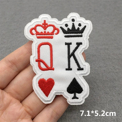 Embroidered patch with 'Q' and 'K' symbols held in a hand on a gray background