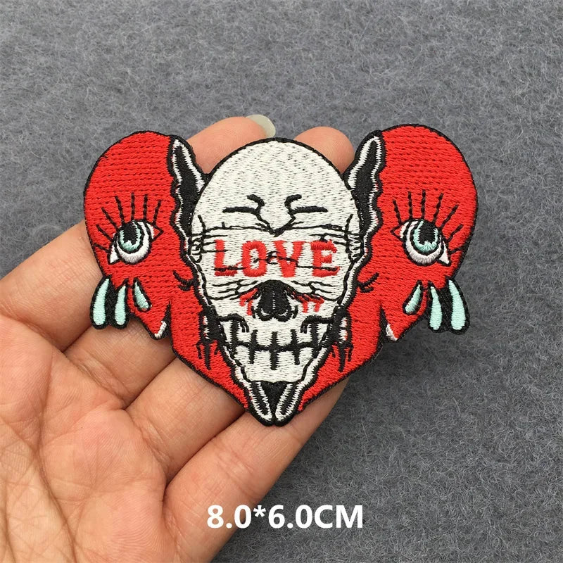 Skull patch with red hearts and 'LOVE' text held in a hand on a gray background