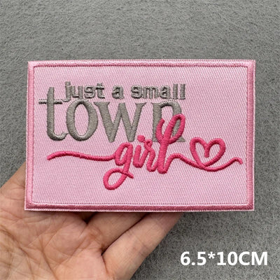 Pink embroidered patch with text held by a hand on a gray background