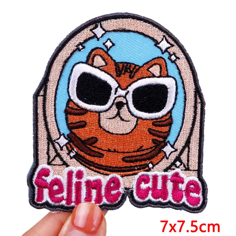 Patch with a cat wearing sunglasses and 'feline cute' text, held by a hand.