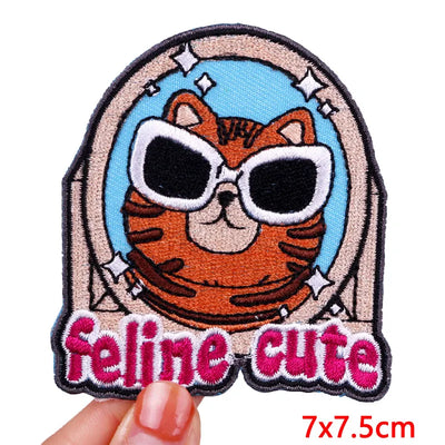 Patch with a cat wearing sunglasses and 'feline cute' text, held by a hand.