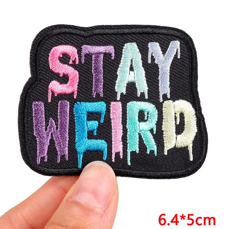 Embroidered patch with 'Stay Weird' text in colorful letters held by a hand.