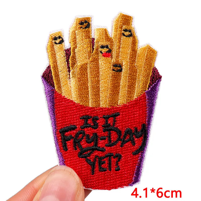 Embroidered patch of French fries with faces in a red box labeled 'Is It Fry-Day Yet?' held by a hand.