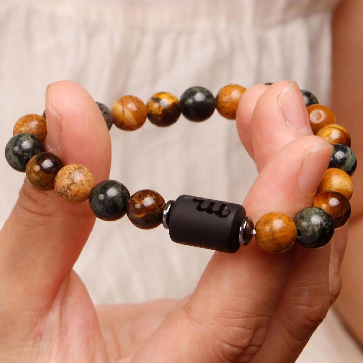Hand holding a beaded bracelet with a focus on the black central bead.
