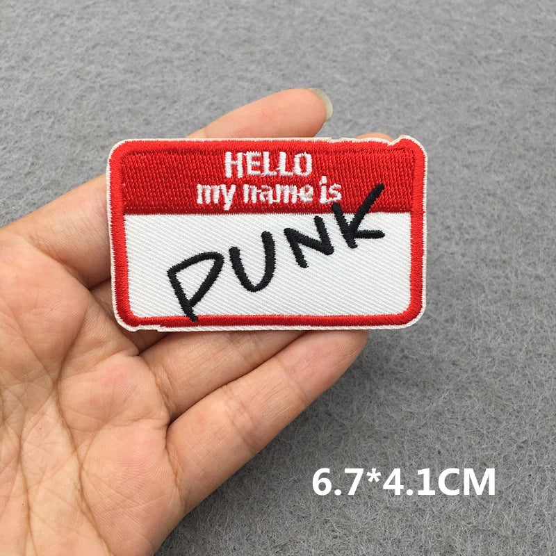 Red and white name tag patch with 'HELLO my name is PUNK' text held in a hand against a gray background.