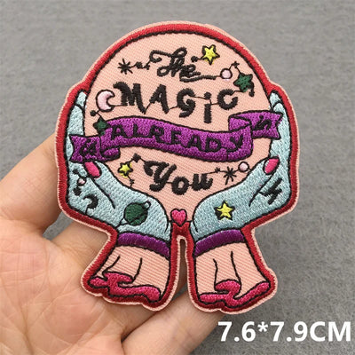 Embroidered patch with text 'The Magic is Already You' held by a hand on a gray background.