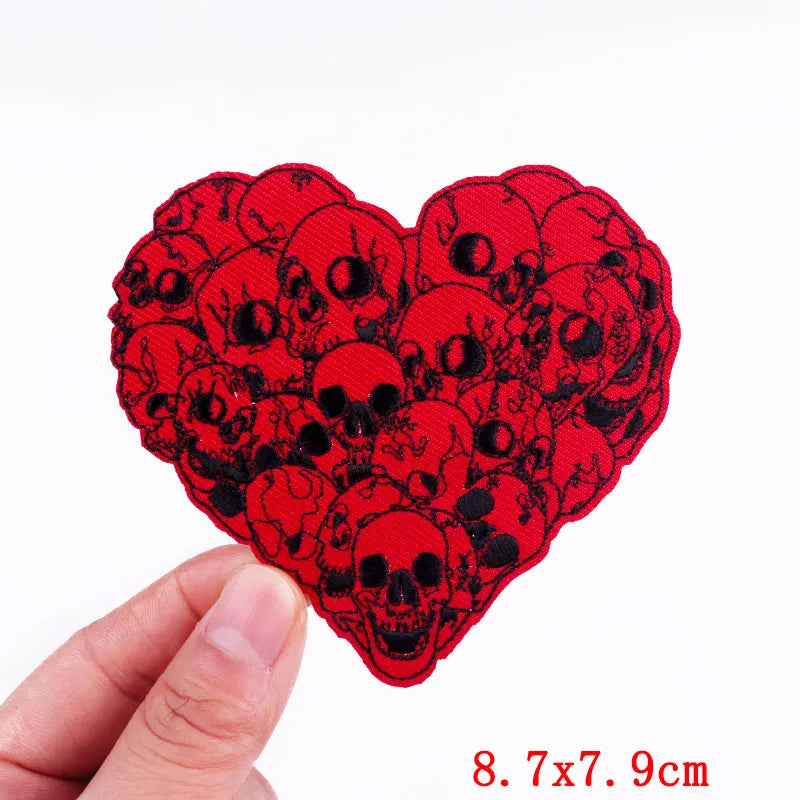 Red heart-shaped patch with black skull design held by a hand on a white background