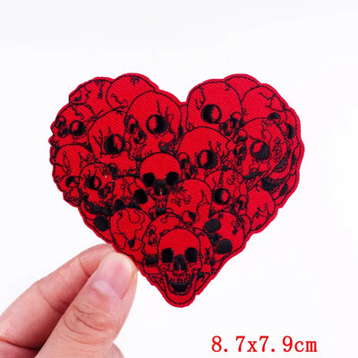 Red heart-shaped patch with black skull design held by a hand on a white background