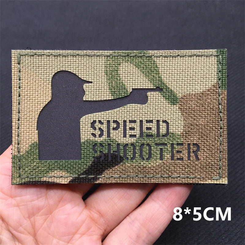 Patch with silhouette of a person shooting and 'SPEED SHOOTER' text on a camouflage background, held in hand.