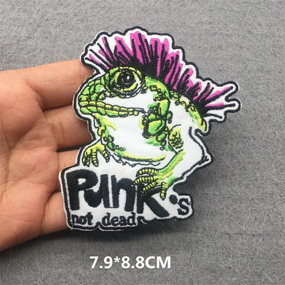 Embroidered patch with a skeleton lizard and mohawk, labeled 'Punk's not dead', held by a hand on a gray background.