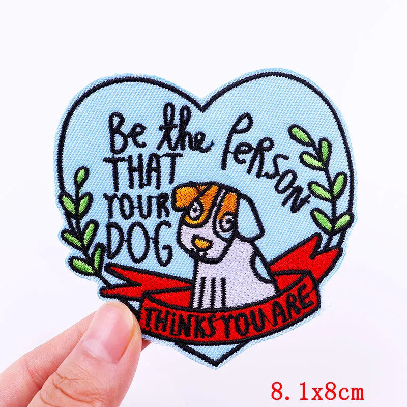 Heart-shaped patch with a dog illustration and text held by a hand on a white background