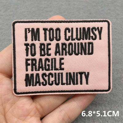 Pink patch with black text held in a hand against a gray background