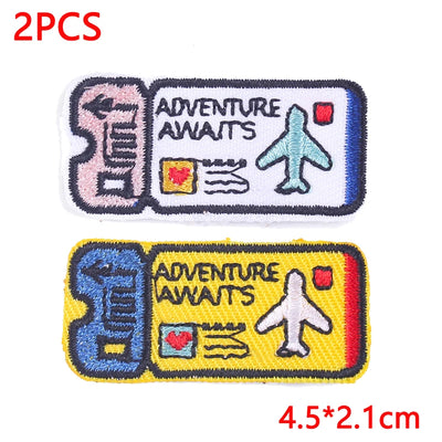 Two embroidered patches with 'Adventure Awaits' text and airplane icon on a white background.