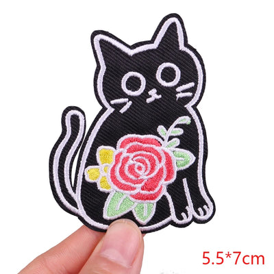 Black cat with a pink rose patch held by a hand on a white background