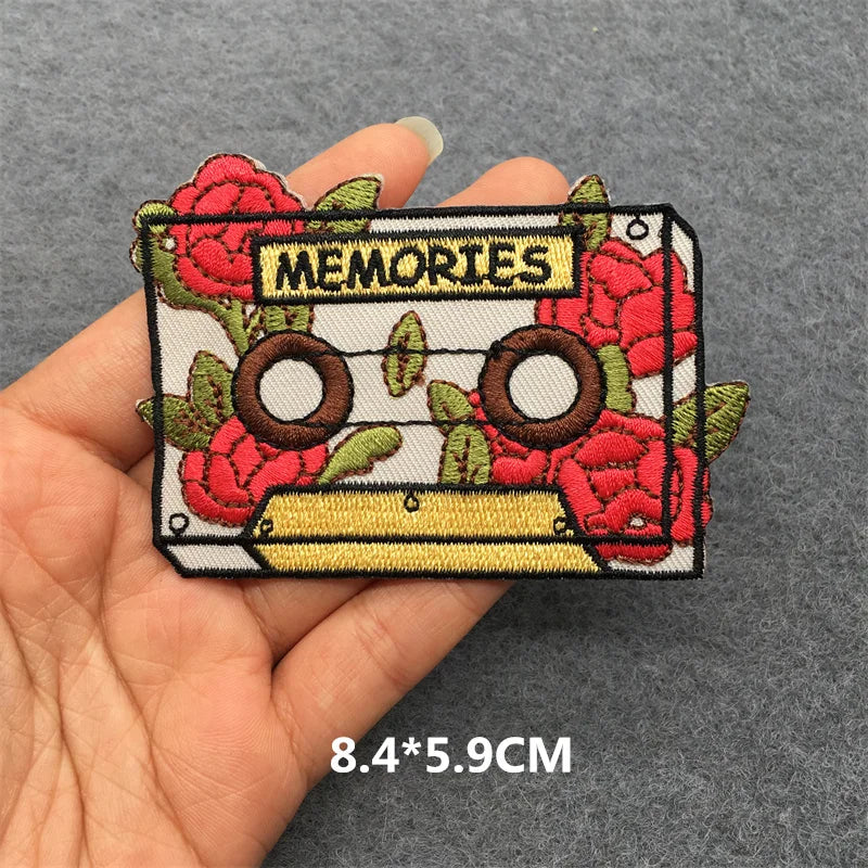 Embroidered patch with cassette tape and roses design held by a hand on a gray background.