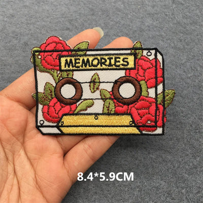 Embroidered patch with cassette tape and roses design held by a hand on a gray background.