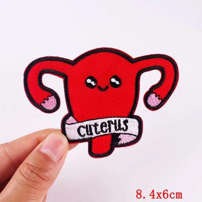 Red cartoon-style uterus patch with 'CUTERUS' text held by a hand on a white background.