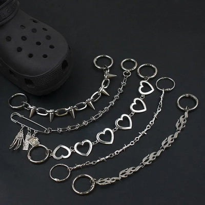 Silver chain for crocs with heart and spike designs on a dark surface.