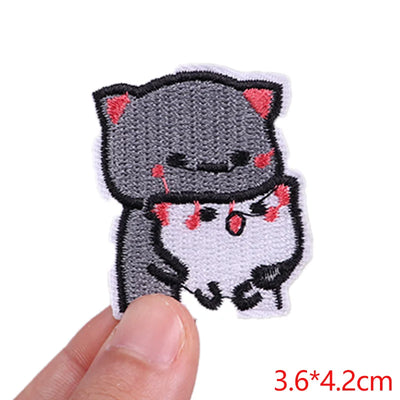 Embroidered patch of a cartoon cat with red accents held by a finger on a white background