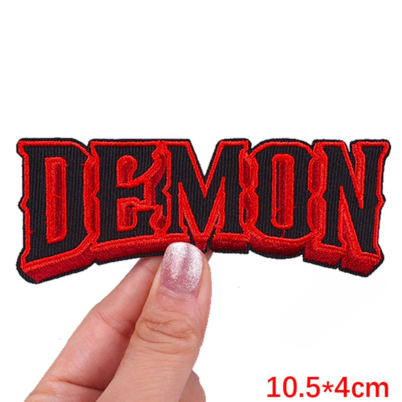Embroidered patch with 'DEMON' text held by a hand on a white background