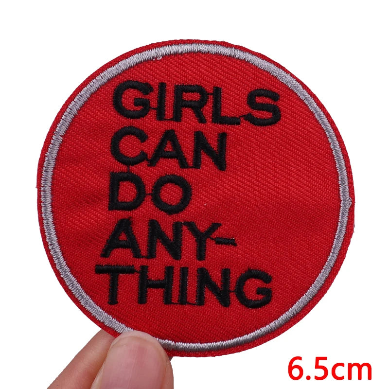Red patch with 'GIRLS CAN DO ANYTHING' text held by a hand, with a measurement label at the bottom right corner.