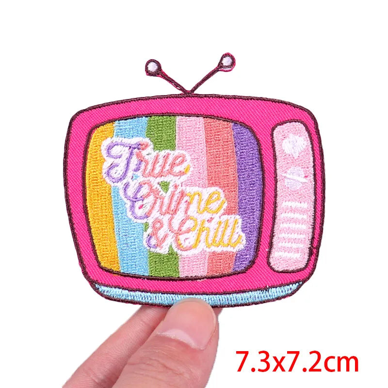 Colorful embroidered patch of a TV with 'Furie Crime & Chilly' text, held by a hand.