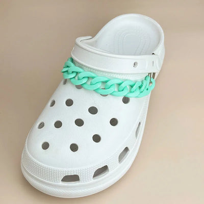 White clog shoe with a turquoise chain strap on a beige background