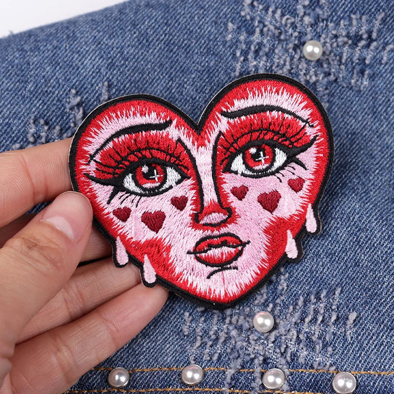 Heart-shaped patch with face design held over denim fabric.