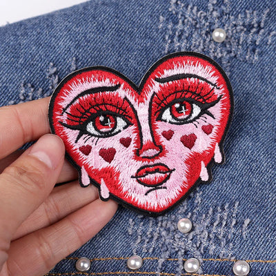 Heart-shaped patch with face design held over denim fabric.