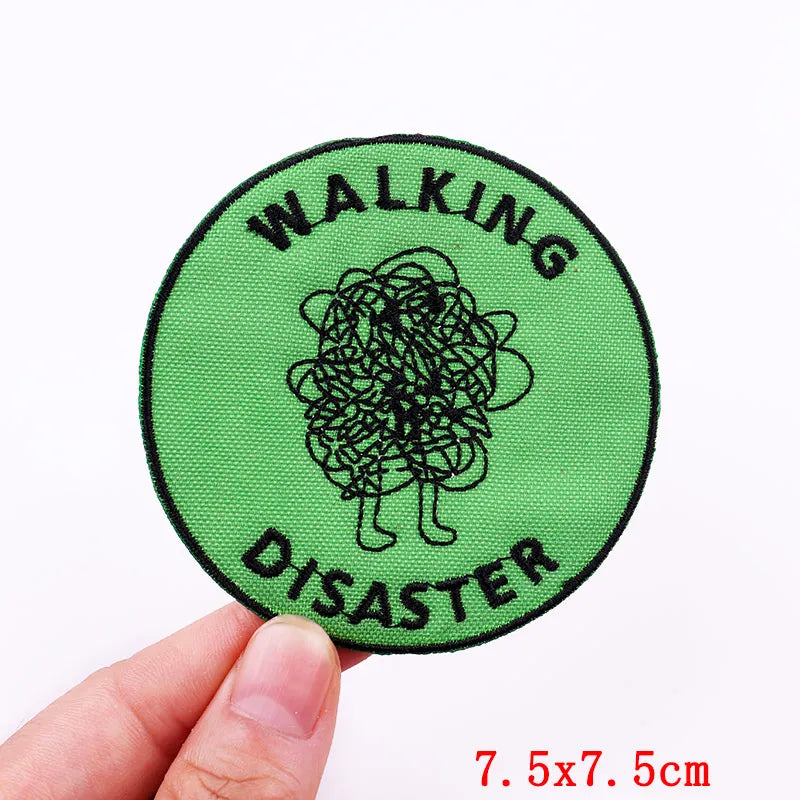 Circular patch with 'Walking Disaster' text and a doodle, held by a hand on a white background.