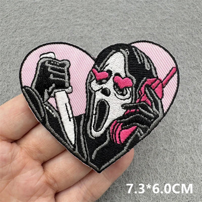 Heart-shaped patch with a stylized face and knife held by a hand on a gray background.