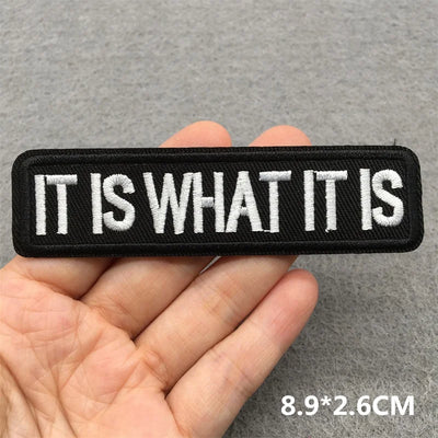 Text patch with 'IT IS WHAT IT IS' held in a hand against a gray background