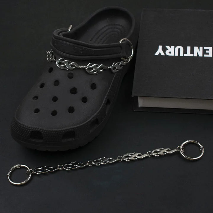 Black clog shoe with a silver chain on a dark surface, featuring the brand &