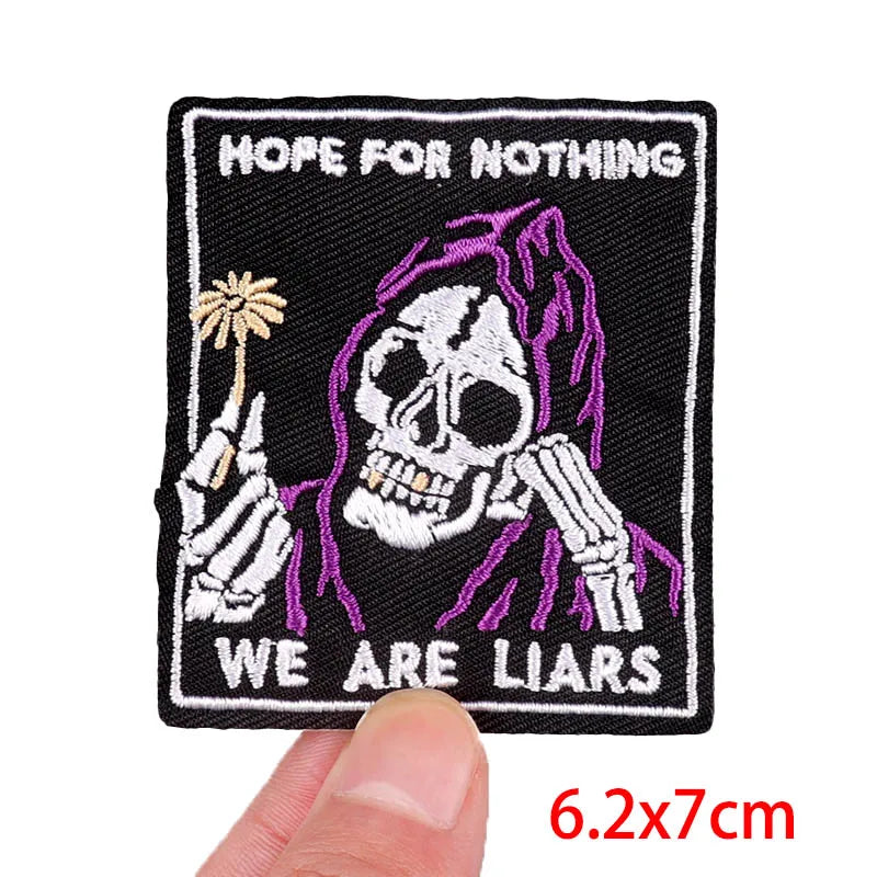 Patch with skeleton holding a palm tree and text 'Hope for Nothing, We Are Liars' held by a hand.