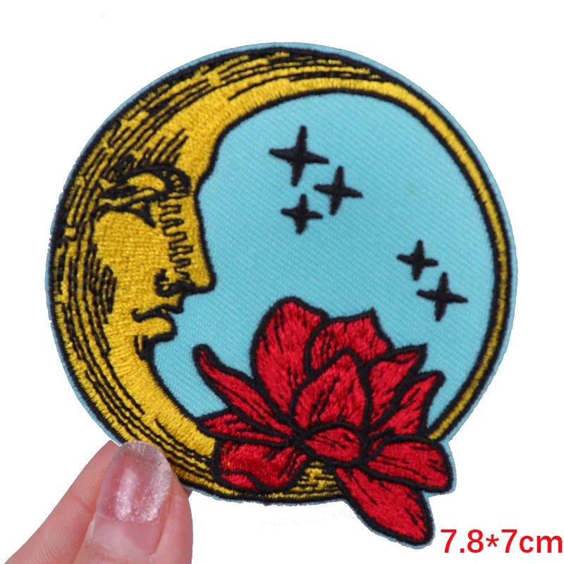 Embroidered patch with moon, stars, and red flower held by a hand on a white background.